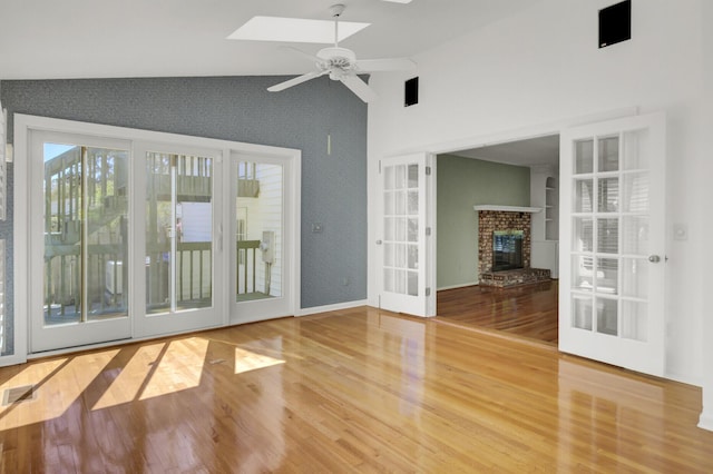 unfurnished living room with ceiling fan, a fireplace, wood finished floors, a skylight, and high vaulted ceiling