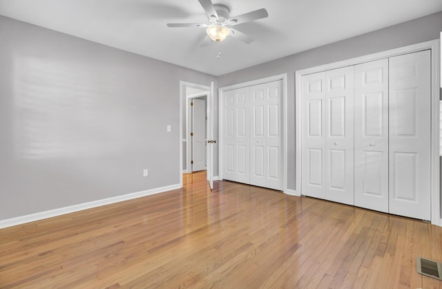unfurnished bedroom featuring baseboards, two closets, a ceiling fan, visible vents, and light wood finished floors