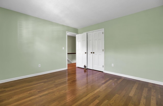 unfurnished bedroom featuring wood finished floors, baseboards, and a closet