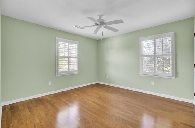 empty room featuring wood finished floors, baseboards, a ceiling fan, and visible vents