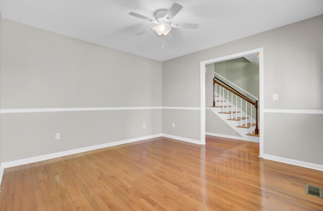 empty room with visible vents, baseboards, a ceiling fan, light wood finished floors, and stairs