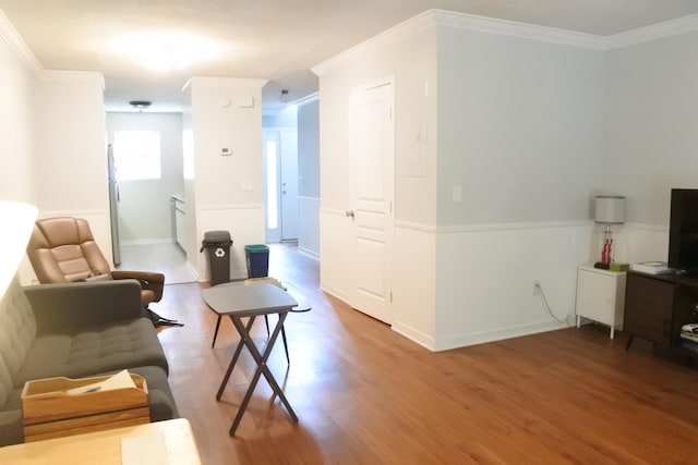 living area with ornamental molding, wood finished floors, and a wainscoted wall