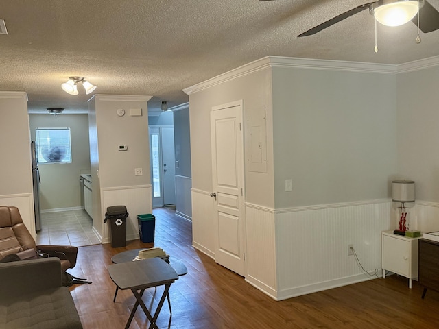 living area with ceiling fan, a textured ceiling, crown molding, wood finished floors, and a wainscoted wall