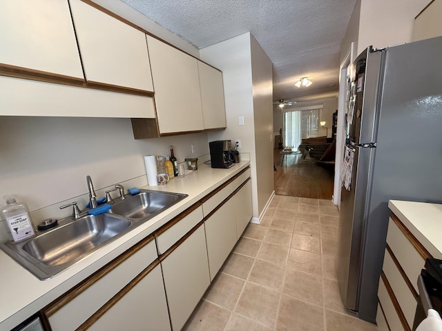 kitchen featuring freestanding refrigerator, light countertops, white cabinets, a sink, and light tile patterned floors