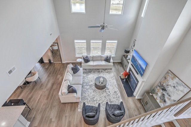 living area featuring ceiling fan, a high ceiling, visible vents, and wood finished floors