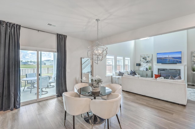 dining space featuring a glass covered fireplace, visible vents, light wood-style flooring, and a chandelier