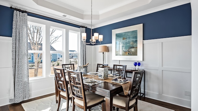 dining space with a notable chandelier, hardwood / wood-style flooring, ornamental molding, and a raised ceiling