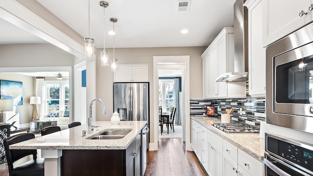 kitchen with appliances with stainless steel finishes, white cabinetry, sink, light stone countertops, and a center island with sink