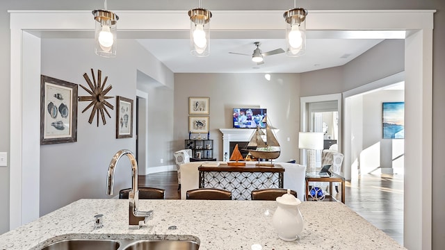 kitchen featuring sink, hardwood / wood-style flooring, ceiling fan, hanging light fixtures, and light stone counters