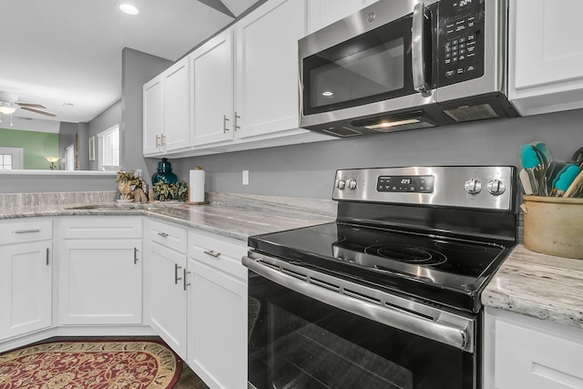 kitchen featuring appliances with stainless steel finishes, white cabinetry, light stone counters, and sink