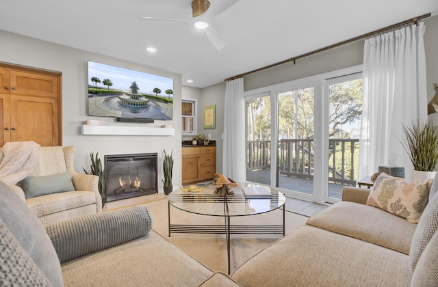 living room featuring recessed lighting, light wood-style flooring, a ceiling fan, and a glass covered fireplace