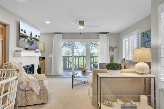 carpeted living area featuring a ceiling fan and a glass covered fireplace