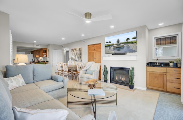 living area featuring recessed lighting, visible vents, a ceiling fan, a glass covered fireplace, and light carpet