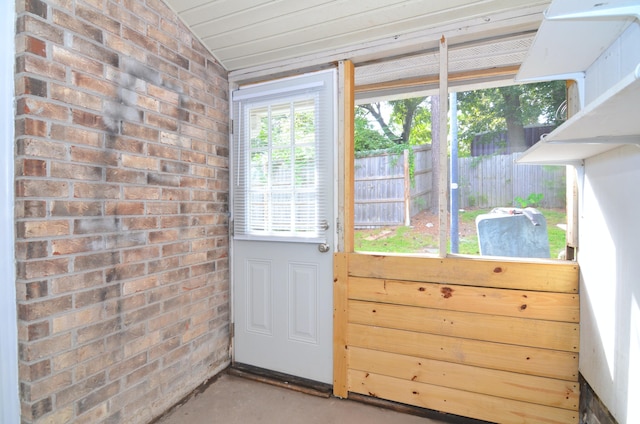 entryway with brick wall, vaulted ceiling, and concrete flooring