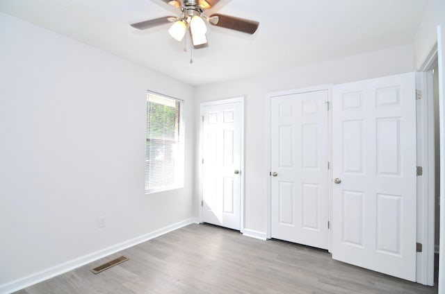 unfurnished bedroom with hardwood / wood-style floors, ceiling fan, and multiple closets