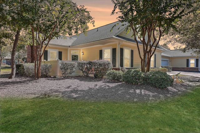 back house at dusk with a garage and a lawn