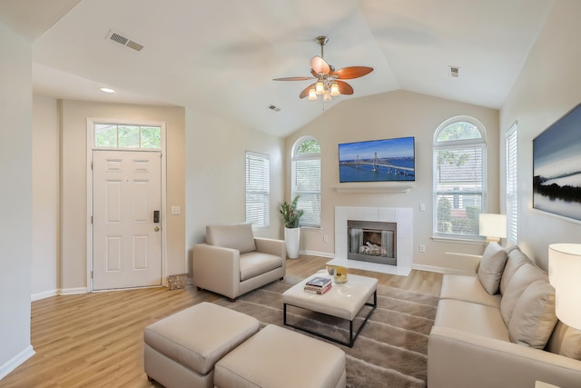 living room with ceiling fan, vaulted ceiling, light hardwood / wood-style floors, and a tile fireplace