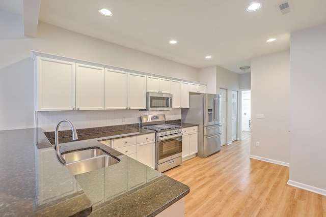 kitchen featuring white cabinets, sink, dark stone counters, appliances with stainless steel finishes, and light wood-type flooring