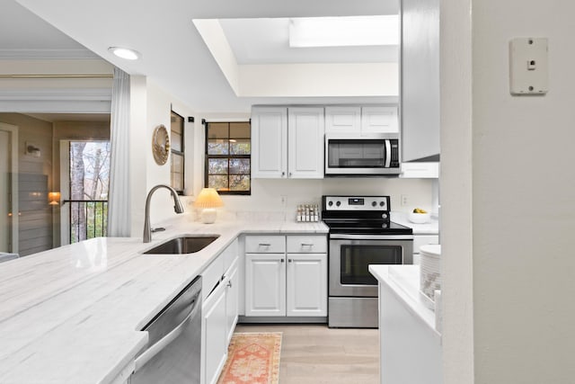 kitchen with appliances with stainless steel finishes, sink, white cabinets, and light hardwood / wood-style flooring