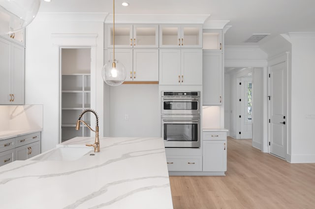 kitchen with white cabinets, hanging light fixtures, light stone countertops, double oven, and light hardwood / wood-style floors