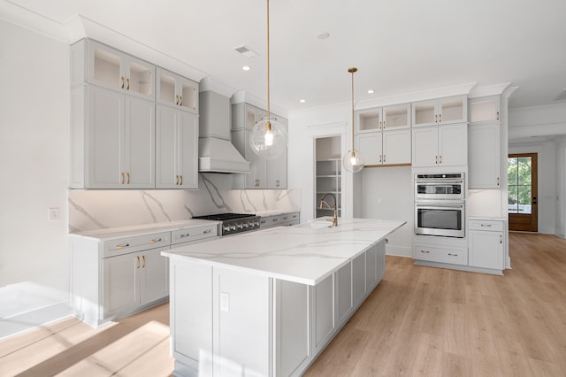 kitchen with sink, stainless steel appliances, pendant lighting, a kitchen island with sink, and custom exhaust hood