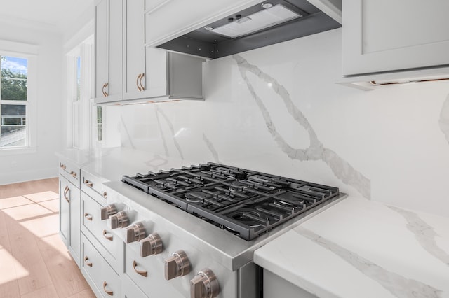 kitchen featuring stainless steel range, light stone counters, light wood-type flooring, custom exhaust hood, and ornamental molding