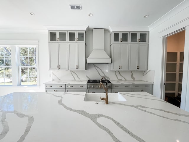 kitchen with premium range hood, sink, stainless steel stove, tasteful backsplash, and light stone counters