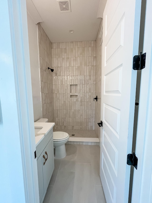 bathroom featuring tile patterned flooring, vanity, toilet, and a tile shower