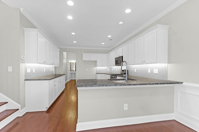 kitchen with a sink, stainless steel microwave, a peninsula, dark stone counters, and recessed lighting