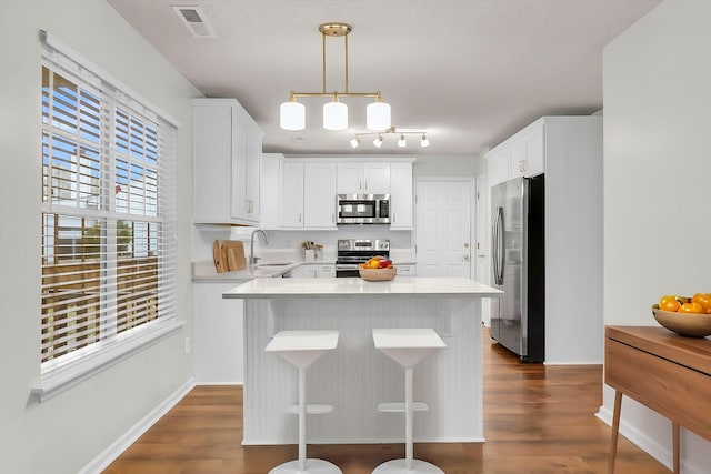 kitchen with sink, hanging light fixtures, a kitchen bar, white cabinets, and appliances with stainless steel finishes