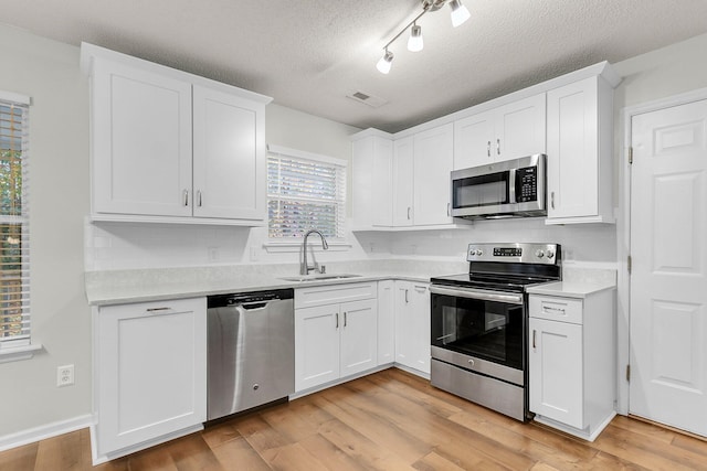 kitchen featuring a textured ceiling, stainless steel appliances, sink, light hardwood / wood-style floors, and white cabinetry