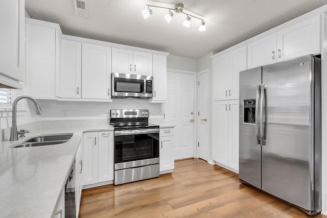 kitchen with appliances with stainless steel finishes, a textured ceiling, sink, white cabinets, and light hardwood / wood-style floors