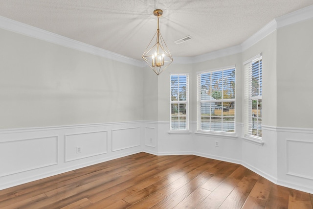 unfurnished dining area featuring hardwood / wood-style floors, ornamental molding, a textured ceiling, and an inviting chandelier