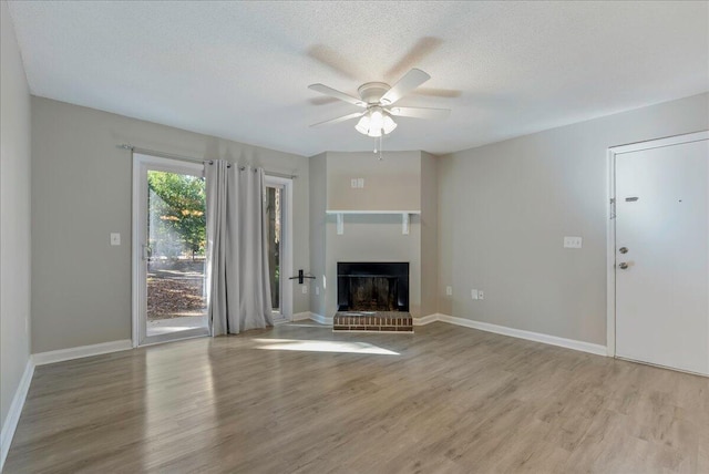 unfurnished living room featuring ceiling fan, light wood-type flooring, a textured ceiling, and a brick fireplace