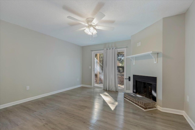 unfurnished living room with hardwood / wood-style floors, ceiling fan, a textured ceiling, and a brick fireplace