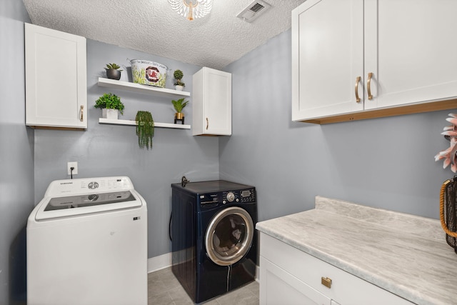 clothes washing area with independent washer and dryer, light tile patterned floors, cabinets, and a textured ceiling