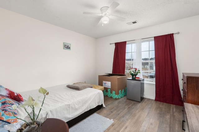 bedroom with stainless steel refrigerator, ceiling fan, light hardwood / wood-style flooring, and a textured ceiling