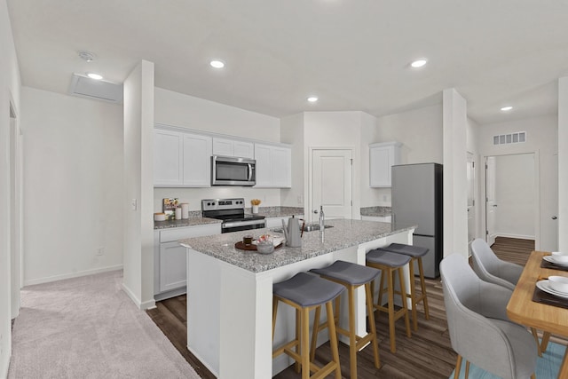 528 Pender Woods Dr, Summerville, SC 29486 - kitchen with appliances with stainless steel finishes, a kitchen island with sink, white cabinetry, a breakfast bar area, and light stone counters