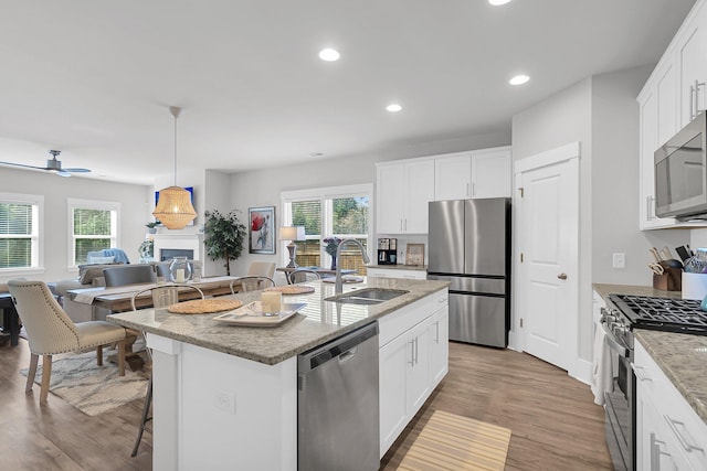 kitchen featuring sink, white cabinetry, light stone counters, a center island with sink, and stainless steel appliances