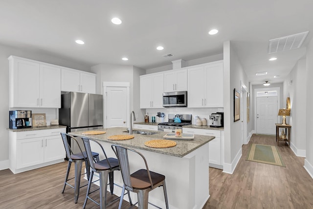 kitchen featuring sink, white cabinetry, light stone counters, a center island with sink, and appliances with stainless steel finishes