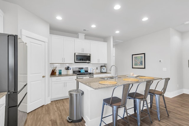 kitchen featuring sink, appliances with stainless steel finishes, a kitchen island with sink, light stone countertops, and white cabinets