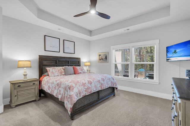 bedroom featuring a tray ceiling, light colored carpet, and ceiling fan