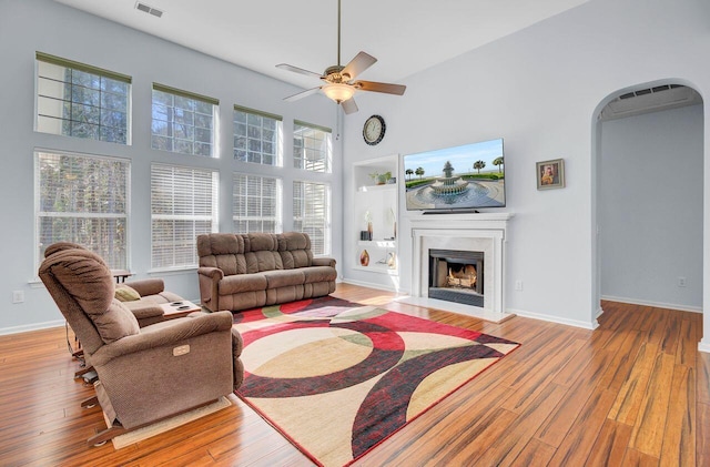 living area featuring baseboards, a fireplace, a high ceiling, hardwood / wood-style flooring, and arched walkways