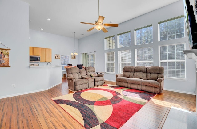 living area featuring baseboards, hardwood / wood-style floors, recessed lighting, a towering ceiling, and a ceiling fan