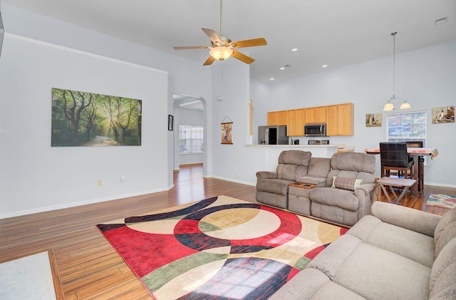 living area featuring a ceiling fan, wood finished floors, arched walkways, and a wealth of natural light