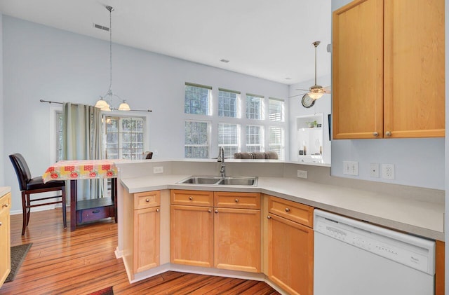 kitchen with a peninsula, a sink, hanging light fixtures, light countertops, and dishwasher