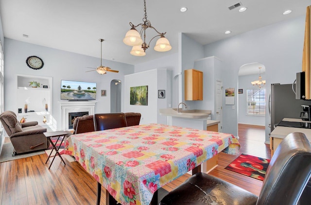 dining area with light wood finished floors, visible vents, ceiling fan with notable chandelier, a fireplace, and arched walkways