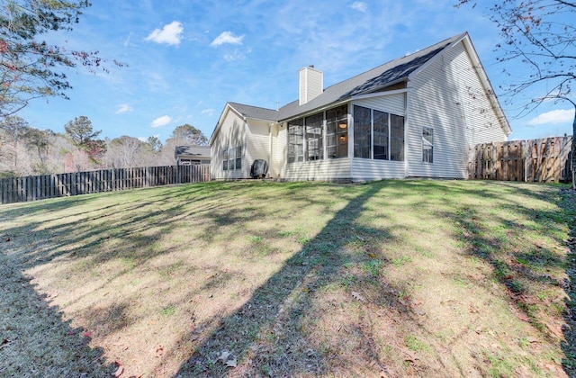 rear view of house with a fenced backyard, a chimney, a yard, and a sunroom