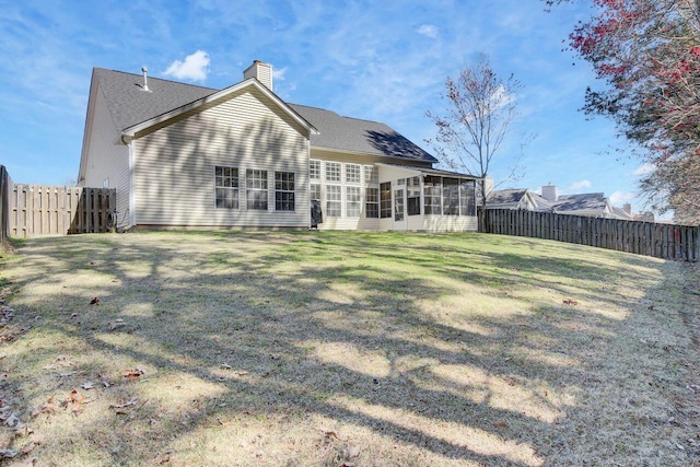 back of house with a yard, a fenced backyard, a chimney, and a sunroom