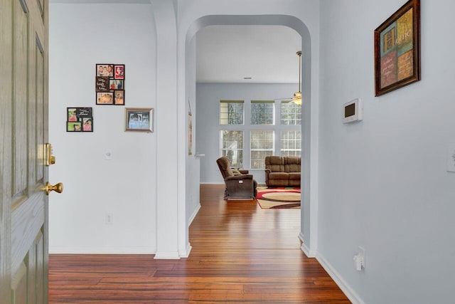 corridor with baseboards, arched walkways, and dark wood-style flooring